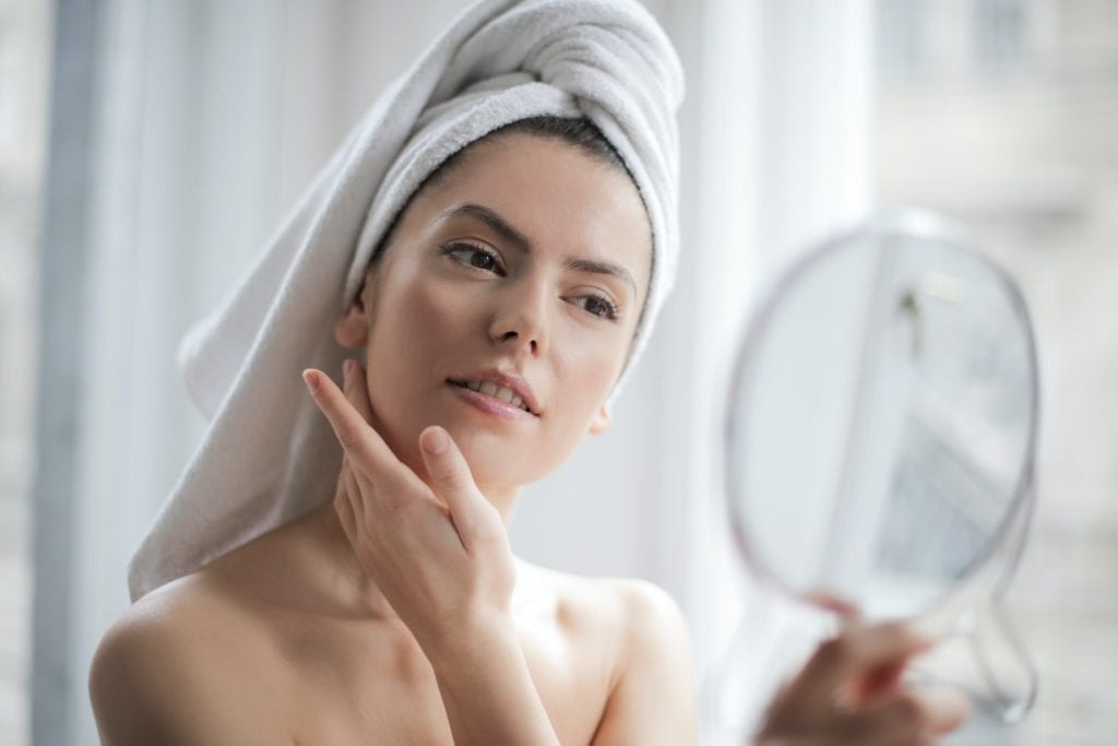 A woman with a towel on her head looks into a mirror